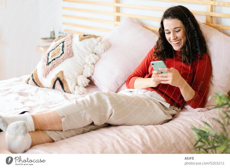 Frau entspannt sich und hat Spaß mit einem Smartphone auf dem Bett jung Handy Technik & Technologie Lachen Glück Lächeln bequem Lügen Freizeit gemütlich