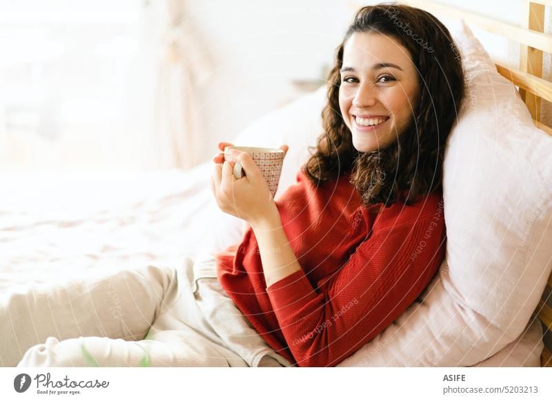 Glückliche Frau mit einem Kaffee auf dem Bett jung Tasse trinken Tee Lächeln bequem Komfort Frühstück aussruhen sich[Akk] entspannen Wohlbefinden genießend