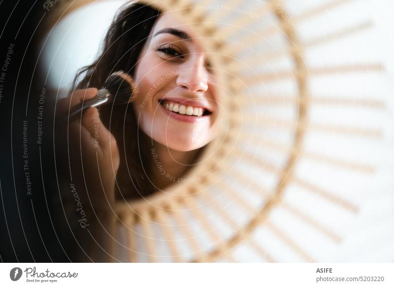 Junge glückliche Frau, die sich vor einem runden Spiegel schminkt jung Bürste Kosmetik anwendend Schminke Lächeln zahnfarben Pulver erröten Gesicht attraktiv