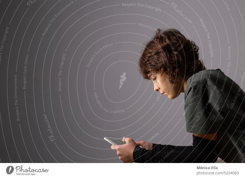 Ein junges Mädchen surft mit einem Tablet oder einem elektronischen Gerät in einem schwach beleuchteten Raum im Internet Teenager T-Shirt dunkel grau schwarz