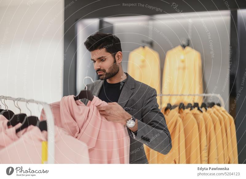 Junger Mann arbeitet in einem Bekleidungsgeschäft Menschen Kleidung Mode Modedesignerin Klient Kleiderstange Konsumverhalten im Innenbereich stylisch Sale