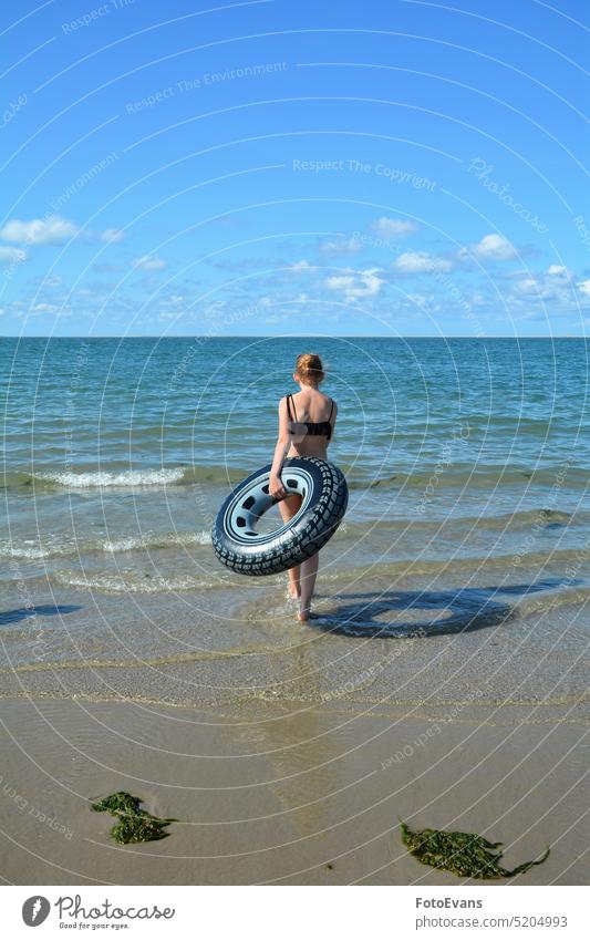 Junges Mädchen von hinten, mit einem Schwimmreifen läuft an einem Sandstrand ins Meer Strand Reise Ferien Ferien & Urlaub & Reisen Küste Tourismus Landschaft