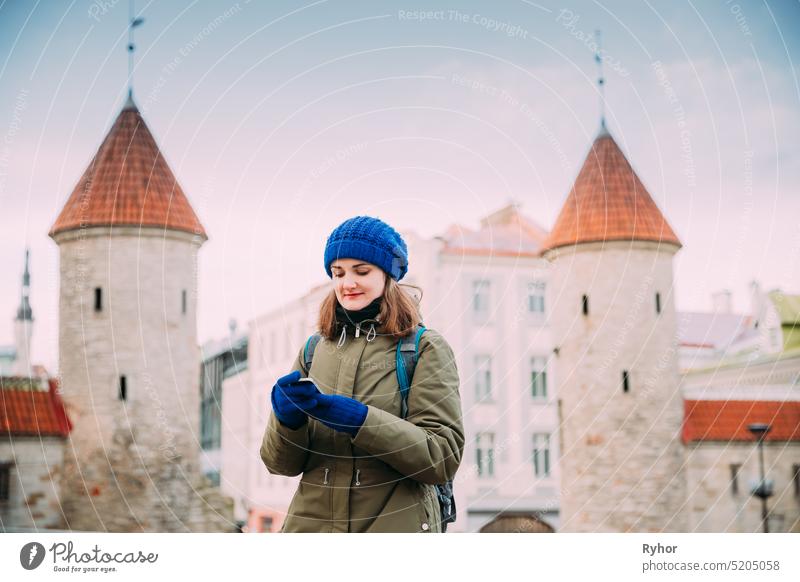 Tallinn, Estland. Junge kaukasische zuversichtlich Frau Backpacker Tourist mit Smartphone in der Nähe Wahrzeichen Viru Tor. Urlaub in der Altstadt. Mädchen Surfen Net Internet in Telefon