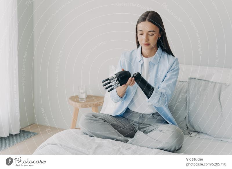 Ein behindertes junges Mädchen zerlegt eine bionische Armprothese und sitzt zu Hause auf dem Bett. Medizinische Technologien Prothesen deaktiviert Arme
