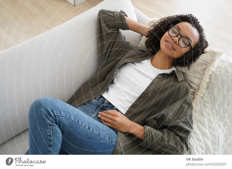 Entspannte heitere junge gemischte Rasse Mädchen ruht auf bequemen Sofa liegen, genießen Nachmittagsschlaf zu Hause Lügen heimwärts Liege Wohnzimmer