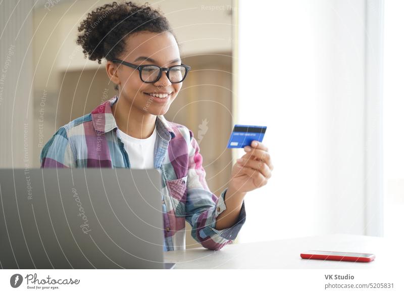 Glückliches afroamerikanisches junges Mädchen, das eine Kreditkarte hält, nutzt Online-Banking-Dienste auf einem Laptop am Schreibtisch Postkarte Afroamerikaner