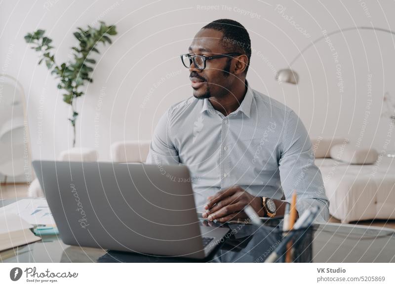 Nachdenklicher afroamerikanischer Geschäftsmann, der an einem Laptop arbeitet und über ein Geschäftsprojekt nachdenkt und zur Seite schaut Afroamerikaner Arbeit
