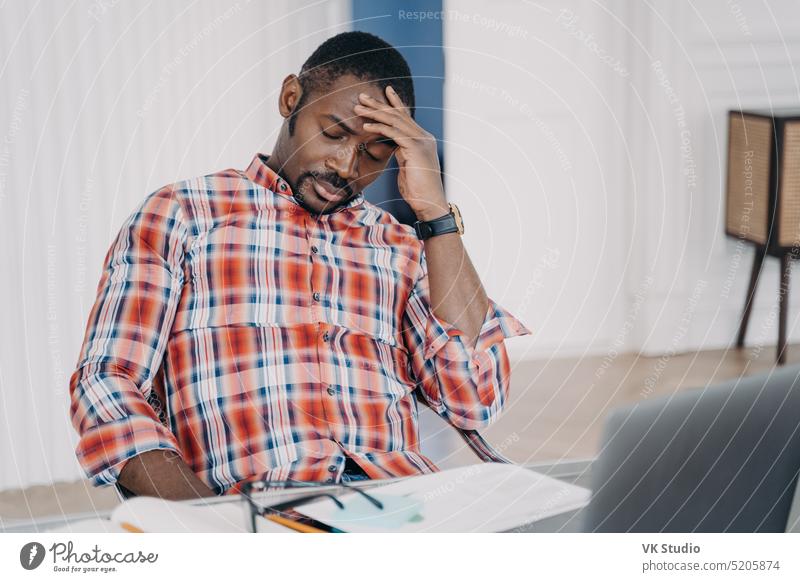 Müder afroamerikanischer männlicher Angestellter, der nach der Arbeit am Laptop unter Kopfschmerzen leidet. Stress bei der Arbeit Afroamerikaner Mann Müdigkeit