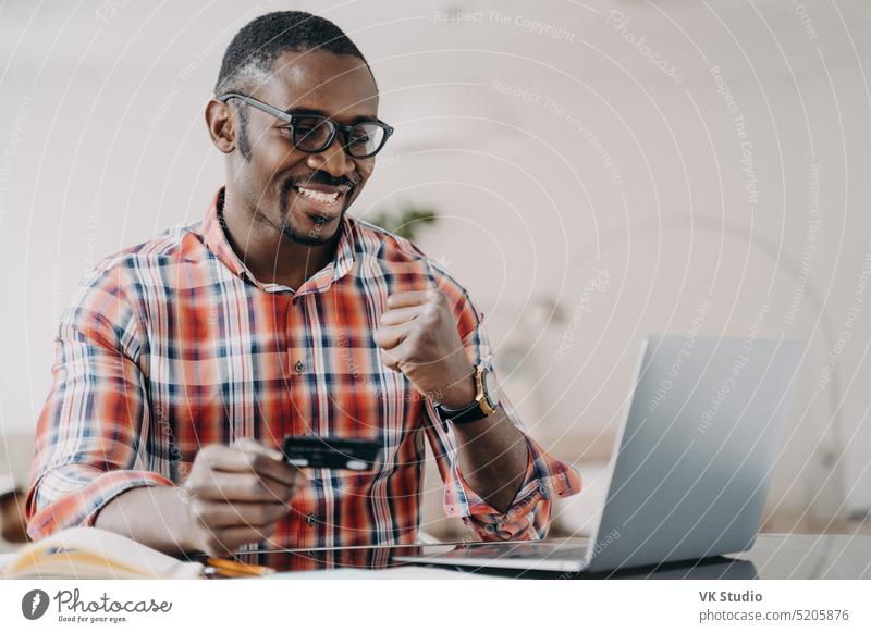 Ein afroamerikanischer Mann, der eine Kreditkarte in der Hand hält, nutzt einen Online-Banking-Dienst am Laptop und macht eine Ja-Geste Afroamerikaner Postkarte
