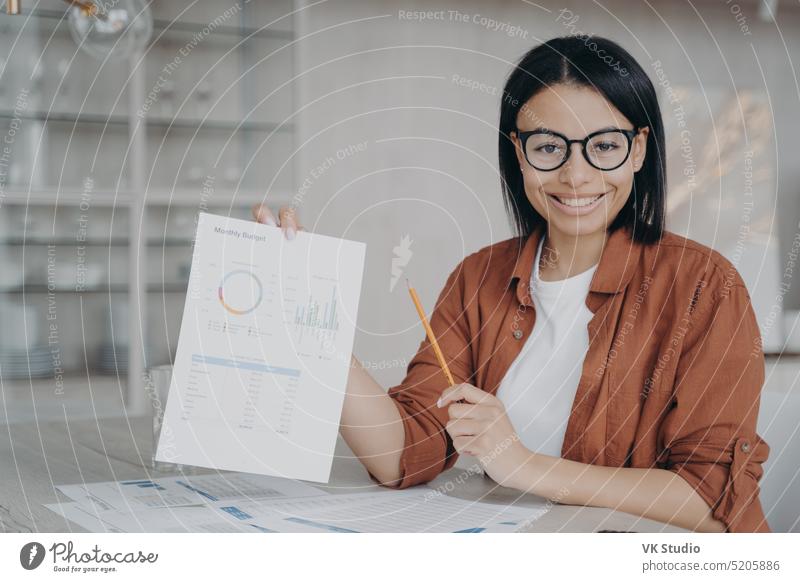 Lächelnde Finanzanalystin zeigt Dokument mit Unternehmensstatistiken, präsentiert Projekt am Schreibtisch freundlich Daten Inbetriebnahme Karriere sitzen