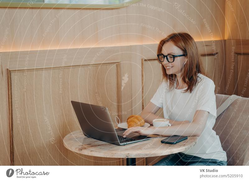 Glücklich lächelnde Frau mit Kopfhörern, die einen Laptop benutzt, während sie in einem Café sitzt Freiberufler freiberuflich Arbeit entfernt Bildung Computer