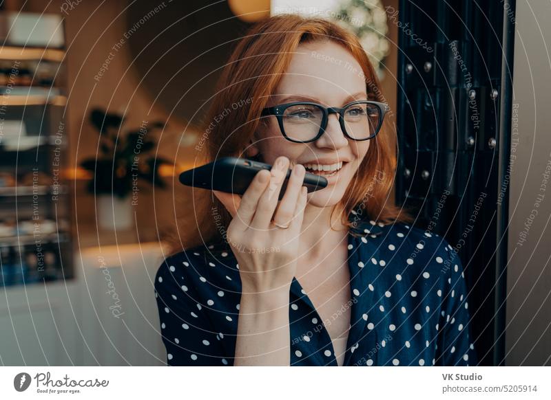 Glücklich lächelnde Geschäftsfrau spricht mit dem Handy über den Lautsprecher beim Verlassen eines Cafés Freisprecheinrichtung Smartphone Audio Aufzeichnen