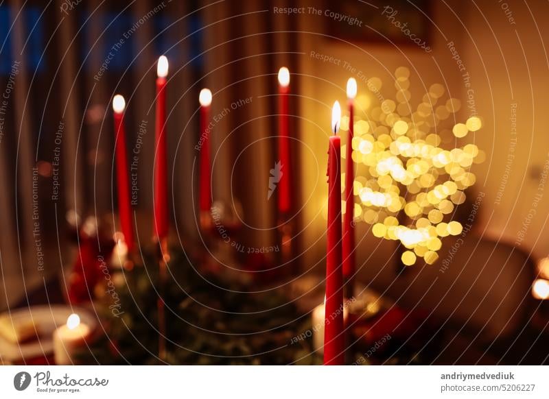 Brennende lange rote Kerzen auf festlichen Tisch für die Feier Weihnachten und Neujahr Feiertage im Wohnzimmer auf Weihnachtsbaum mit Girlanden Hintergrund. Esstisch dekoriert Tannenzweige und Weihnachtskugeln
