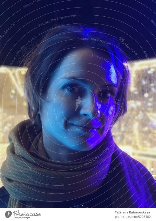 Lila und blaues Neonlicht beleuchtet das Gesicht einer jungen dunkelhaarigen Frau auf gelbem Lichterhintergrund purpur neonfarbig aufleuchten Porträt
