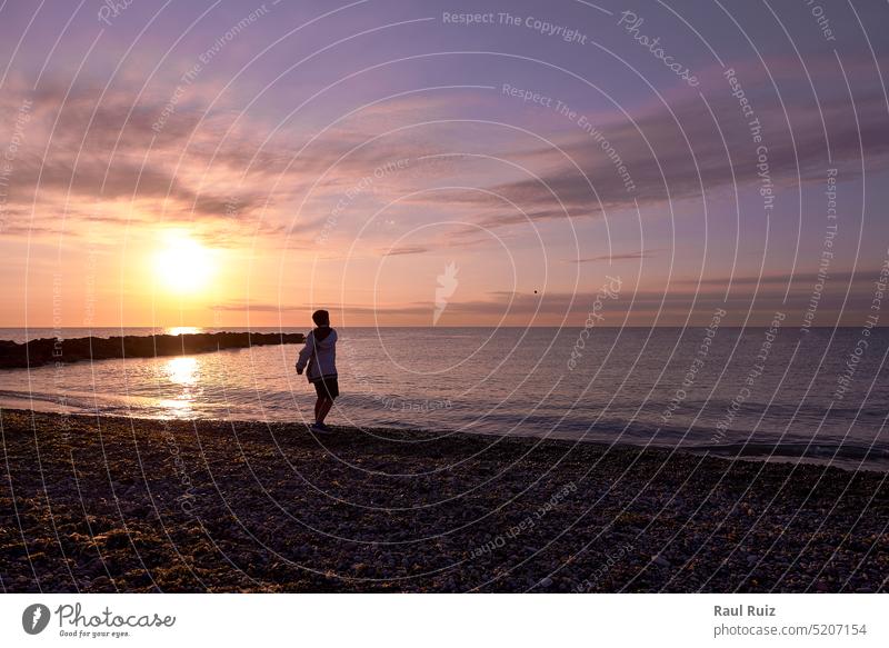 Junge, der in der Morgendämmerung am Strand Kieselsteinchen wirft Abenddämmerung Phantasie Horizont Panorama panoramisch friedlich Reflexion & Spiegelung