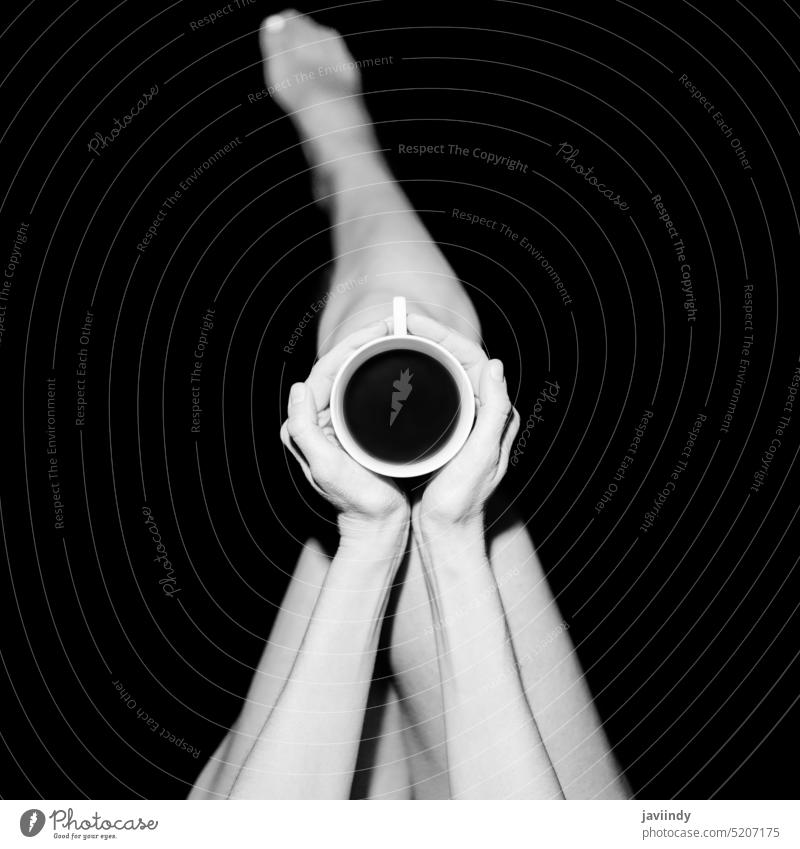 Crop anonyme Frau mit Kaffeetasse in schwarzem Studio sich[Akk] entspannen ruhen Koffein Tasse trinken Getränk Verlockung Bein Barfuß Aroma Heißgetränk genießen