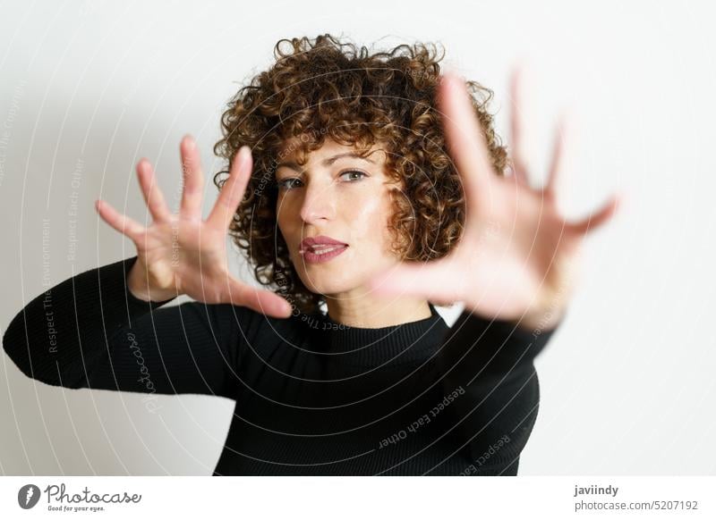 Fokussierte Frau, die ihre Arme ausstreckt und eine Stopp-Geste mit vollständig geöffneten Handflächen zeigt gestikulieren stoppen Zeichen Model krause Haare