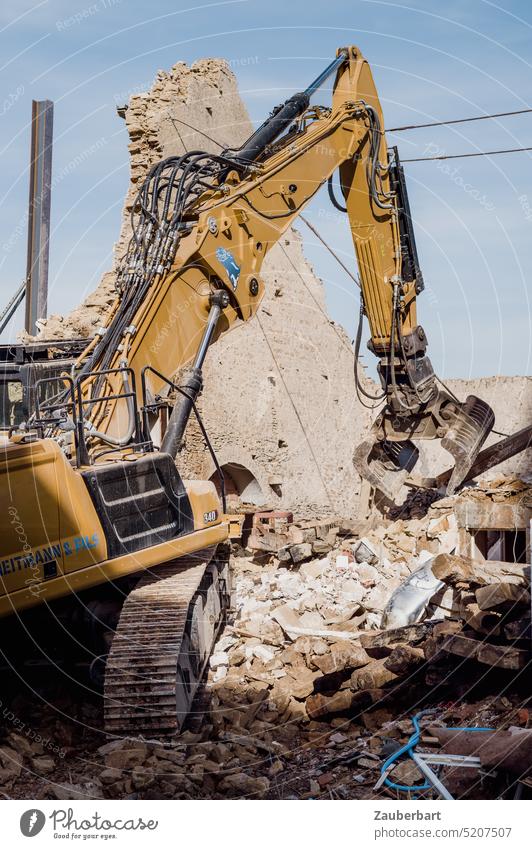 Gelber Bagger reißt ein historisches Haus ab, von dem nur noch die Giebelwand steht Raupenbagger Baumaschine gelb Ruine Trümmer abreißen Zerstörung energisch