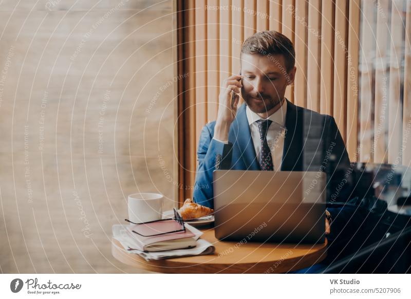 Porträt eines eleganten Finanzmannes im schicken Anzug, der in einem Café mit offenem Laptop sitzt jung Geschäftsmann Anruf reden Mann aus der Ferne Computer