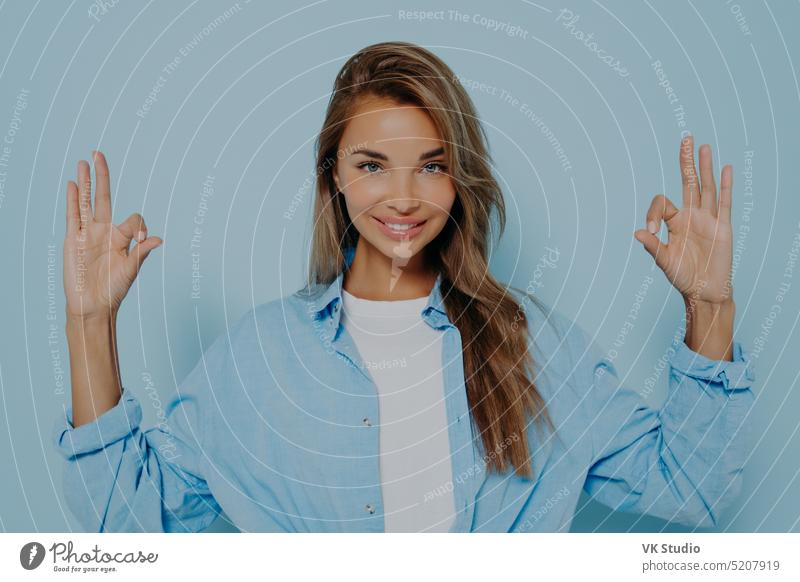 Charmante Frau macht okay Geste gegen hellblauen Hintergrund Ruhe Mudra Kaukasier Mode Gesicht Jugend lange Haare freundlich Schönheit fein Gesichtsausdruck