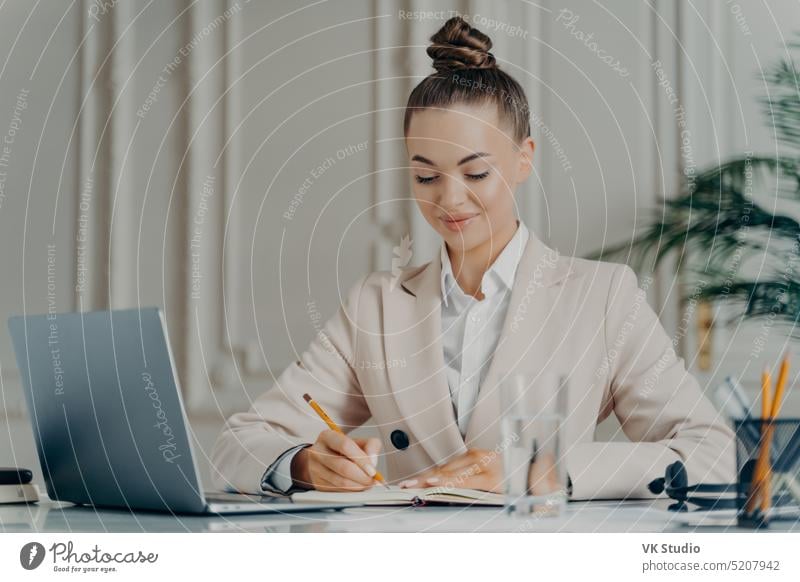 Attraktive erfolgreiche Geschäftsfrau im eleganten Anzug, die bei der Arbeit eine Aufgabenliste erstellt Frau Business Computer Internet Büro