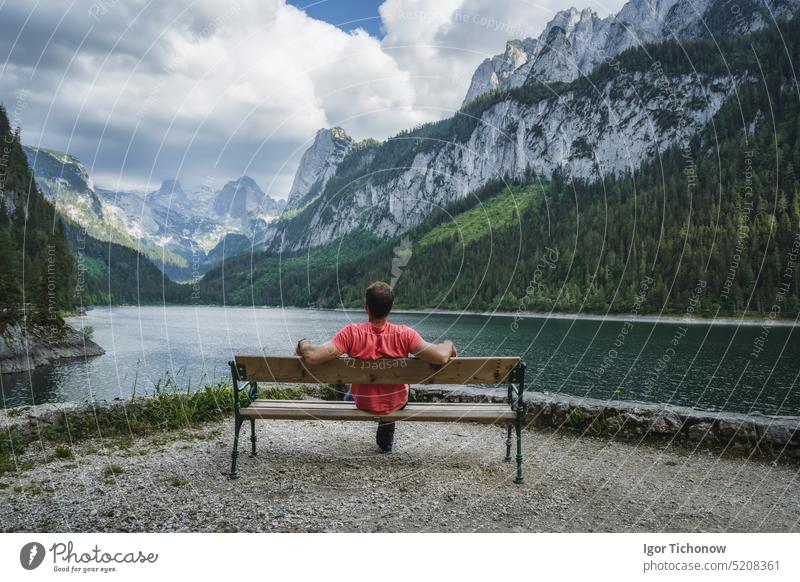 Mann entspannt sich auf einer Bank vor dem Dachstein-Gebirge, das sich im Gosauer See spiegelt, Österreich männlich Berge Natur Landschaft reisen Alpen Wasser