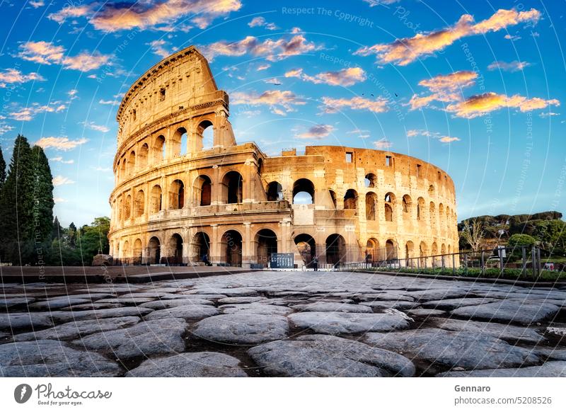 Das Kolosseum bei Sonnenuntergang in Rom, Italien. Tiefblick auf die Hauptfassade des Kolosseums und, im Vordergrund, die antike Pflasterung aus polierten Steinplatten.