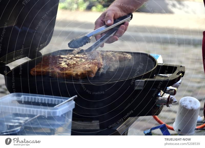 Street Food ist im Kommen - Meisterhand mit Wendezange beim Fleisch braten und wenden auf einem Propangas Grill draußen an der Straße grillen Fleisch grillen