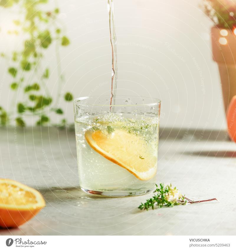 Gesundes Getränkekonzept mit Wasserglas, Kräutern und Orangenscheiben auf hellem Tisch. Frontansicht gesundes Getränk Küchenkräuter Orangenscheibchen Konzept