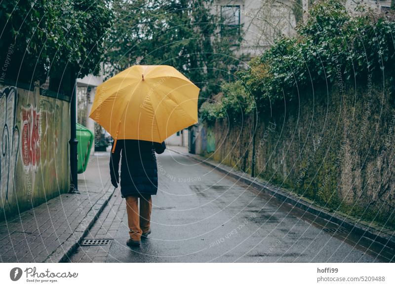 Mensch mit großem gelben Regenschirm geht die Straße hinunter nass schlechtes Wetter Schutz Schirm Gedeckte Farben kalt feucht Regenwetter grau
