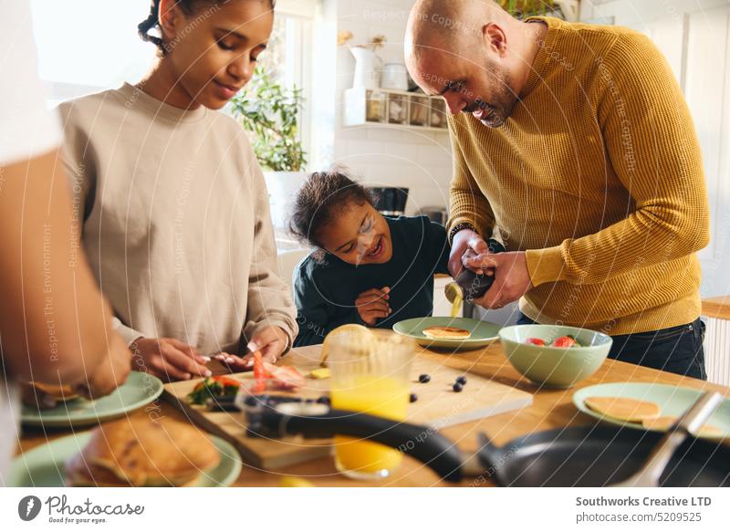 Junge mit Down-Syndrom isst Pfannkuchen zum Frühstück mit seiner Familie rassenübergreifend dienen essen eingießen Sirup Eltern vier schwarz Küche Lebensmittel