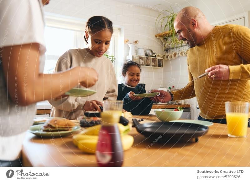 Familie und Junge mit Down-Syndrom servieren Pfannkuchen zum Frühstück essen dienen Eltern schwarz Küche Lebensmittel rassenübergreifend machen Lachen Freude