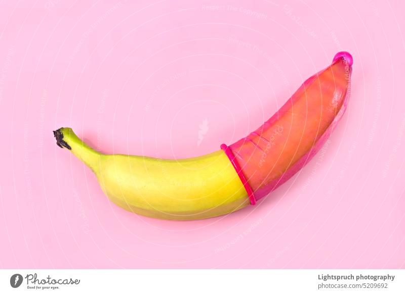 Rotes Kondom auf Banane mit rosa Hintergrund. Safe Sex Konzept. Symbol Sexualerziehung sexuelle Fragen AIDS Verhütungsmittel Erektion