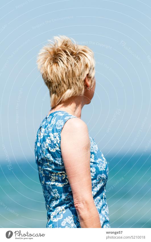 Eine mit einem blauweißen Kleid gekleidete blonde Frau schaut auf das ferne Meer Sommer Sonne Sonnenschein Blonde Haare Ostsee blau/weiß blauweißes Kleid
