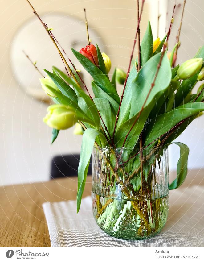 Glasvase mit Tulpen auf Esstisch Vase Blumenstrauß Frühling Ostern Wohnzimmer Esszimmer Tisch Deko Innenaufnahme Unschärfe grün rot gelb Spiegel Zweige Blätter
