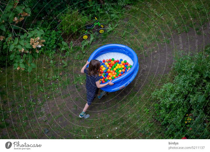 Kind trägt Bällchenbad durch den Garten Mädchen tragen Kindheit bunte Bälle spielen Spielzeug aufblasbar Planschbecken Sommer mehrfarbig Vogelperspektive