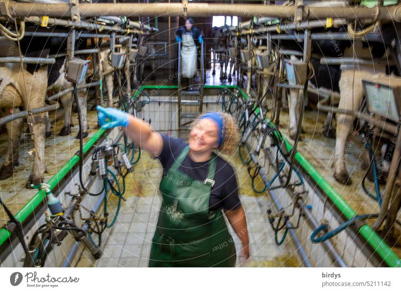 Lustige Bäuerin in einem Melkstand für Milchkühe Landwirtschaft Kühe Milchproduktion Lächeln zeigen Milchviehbetrieb Blick in die Kamera Bauernhof Melkanlage
