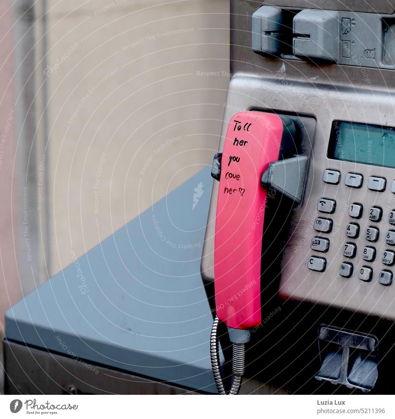 Öffentlich gemachte Gefühle: Tell her you love her mit Ausrufezeichen am rosa Telefonhörer Telefonzelle Fernsprecher Fernsprechapparat Hörer Botschaft Herz