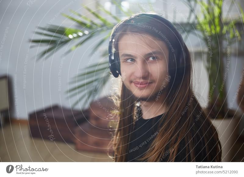 Porträt eines jungen Mannes mit langen Haaren, der zu Hause Kopfhörer trägt Schüler online Musik heimwärts hören lange Haare Person männlich Typ Internet Arbeit