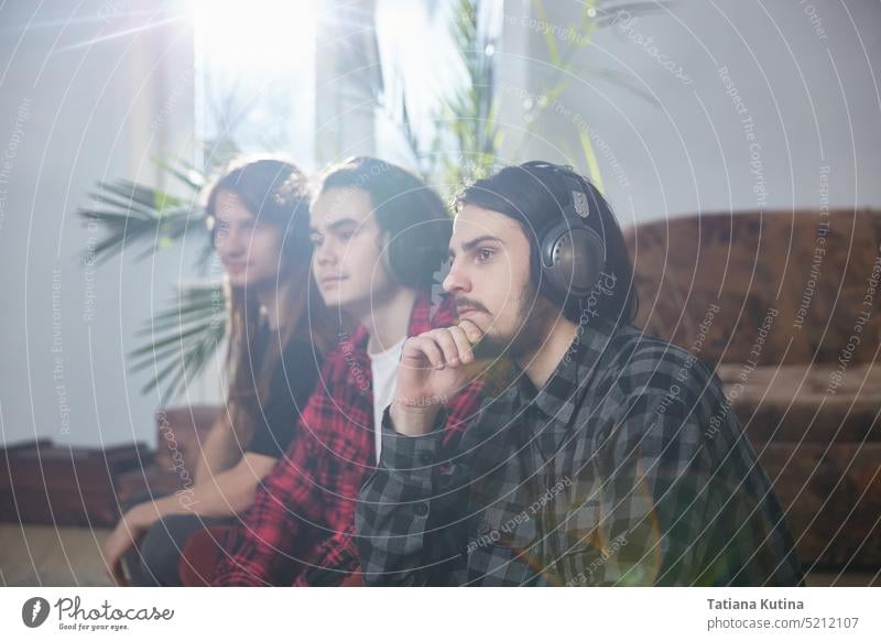 Drei Männer mit Mobiltelefonen und Kopfhörern genießen Musik zu Hause. Eine Gruppe von drei jungen Menschen fühlt sich frei und genießt das Leben Musiker