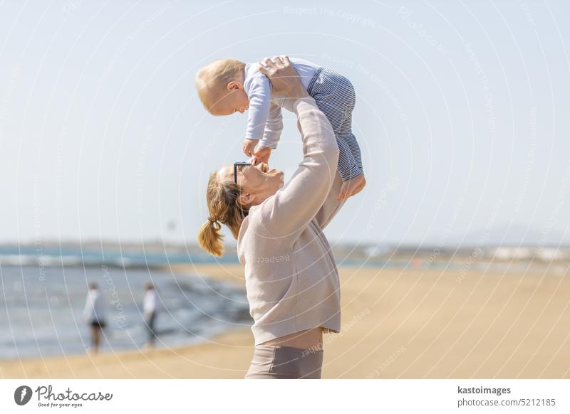 Mutter genießt Sommerferien halten, spielen und heben sein Kleinkind Junge Sohn hoch in die Luft auf Sandstrand auf Lanzarote Insel, Spanien. Familie Reisen und Urlaub Konzept