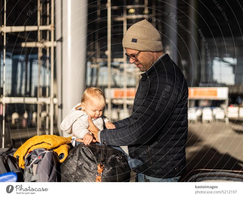 Fatherat tröstet seine müde Säugling Junge Kind sitzt auf der Oberseite des Gepäcks Wagen vor dem Flughafen-Terminal Station während der Reise wih Familie.
