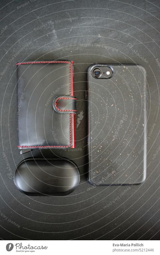 Smartphone, Kopfhoerer und minimalistischer Geldbeutel in schwarz vor schwarzem Grund, Inhalt einer Maennertasche, Lifestlye Flatlay in schwarz und rot brown