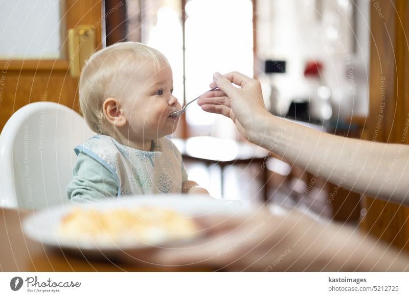 Mutter Löffel füttern ihr Kleinkind Junge Kind sitzt in Hochstuhl am Esstisch in der Küche zu Hause Baby Lebensmittel Pflege Säugling heimwärts Familie hungrig