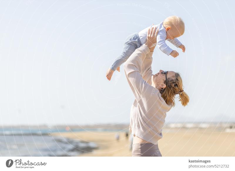 Mutter genießt Sommerferien halten, spielen und heben sein Kleinkind Junge Sohn hoch in die Luft auf Sandstrand auf Lanzarote Insel, Spanien. Familie Reisen und Urlaub Konzept.