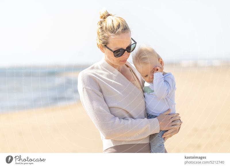 Mutter hält und trägt sein Kleinkind Junge Sohn auf Sandstrand genießen Sommerferien auf der Insel Lanzarote, Spanien. Familie Reisen und Urlaub Konzept. Ferien