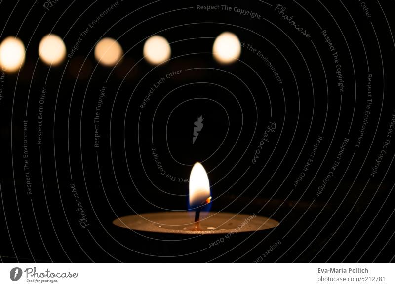 kleines Teelicht vor schwarzem Hintergrund und Lichtreflexen, Kerze der Anteilnahme, Glaube und Hoffnung in schweren Zeiten trauerfeier ende hintergrund traurig