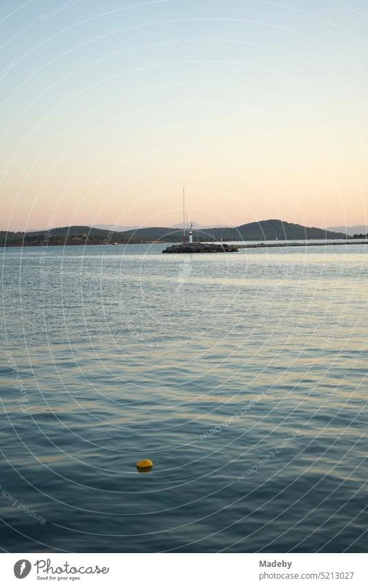 Romantische Abendstimmung am Meer mit dem Licht der Abendsonne mit Leuchtturm und Pier am Hafen in der Bucht von Ayvalik am Ägäischen Meer in der Provinz Balikesir in der Türkei