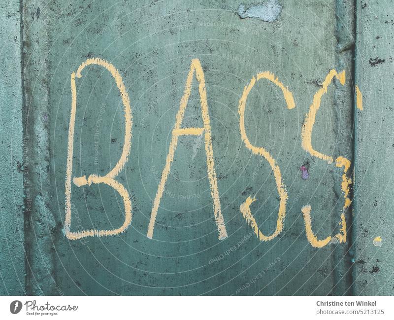 Das Wort "BASS" wurde in hellem Gelb an eine graugrüne Fassade geschrieben Bass Graffito Schrift Musik Musikinstrument Schriftzeichen Schmiererei Typographie