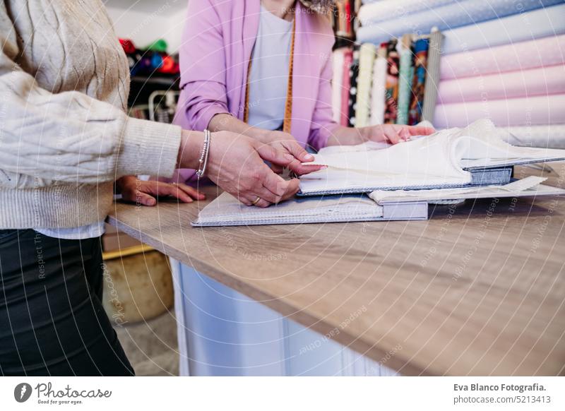 Ältere Frau arbeitet in einem Atelier mit Kundenvorführung und Stoffproben. Kleines Geschäft Kleinunternehmen Werkstatt Senior Mann Stoffe bügelnd arbeiten Job